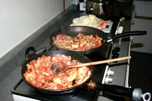 Drei riesige Pfannen Bratkartoffeln mit Zwiebeln, Tomaten und Eiern.